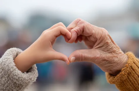 Kinderhand und die Hand einer alten Person bilden zusammen ein Herz