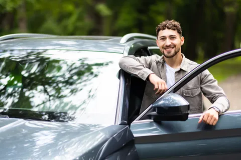 Ein junger Mann steht neben einer geöffneten Autotür.