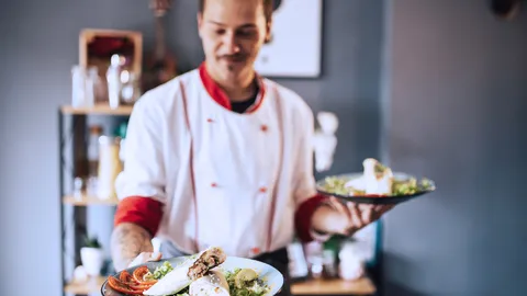 Ein Koch in Arbeitskleidung zeigt Teller mit Essen