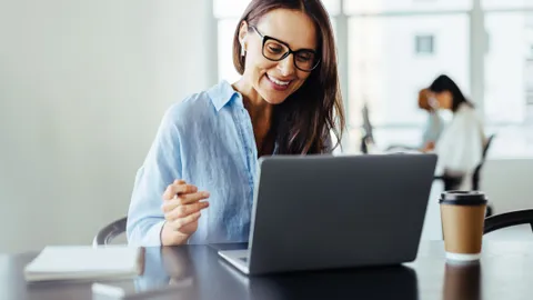 Frau am Tisch blickt zufrieden in ihren Laptop