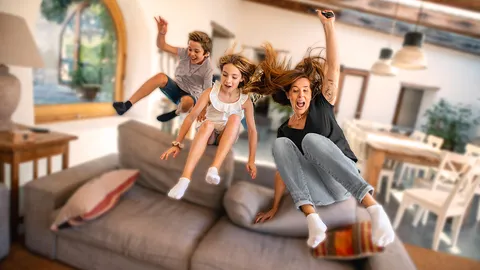 Mutter und Kinder springen auf eine Couch im Wohnzimmer.