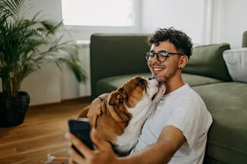 Junger Mann sitzt mit seinem Hund gemütlich im Wohnzimmer vor der Couch auf dem Boden
