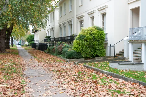 Mit Herbstlaub bedeckter Fußweg vor georgianisch terrassierter Häuserzeile In Cheltenham, England