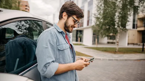 Junger Mann lehnt an einem Wagen und schaut auf sein Handy