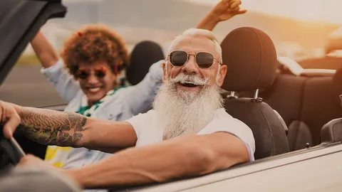 Junge Frau und älterer Mann mit Bart und Sonnenbrille fahren im Cabrio