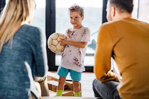 Ein Junge mit einem Fußball beichtet seinen Eltern etwas.