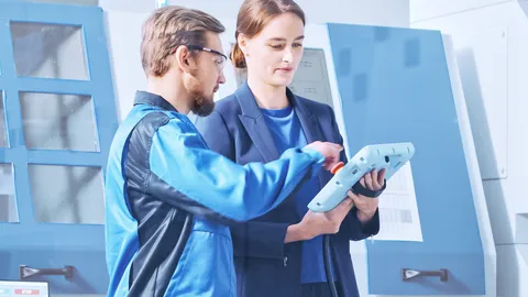 Ein Mann und eine Frau stehen in Arbeitskleidung in einer Fertigungshalle